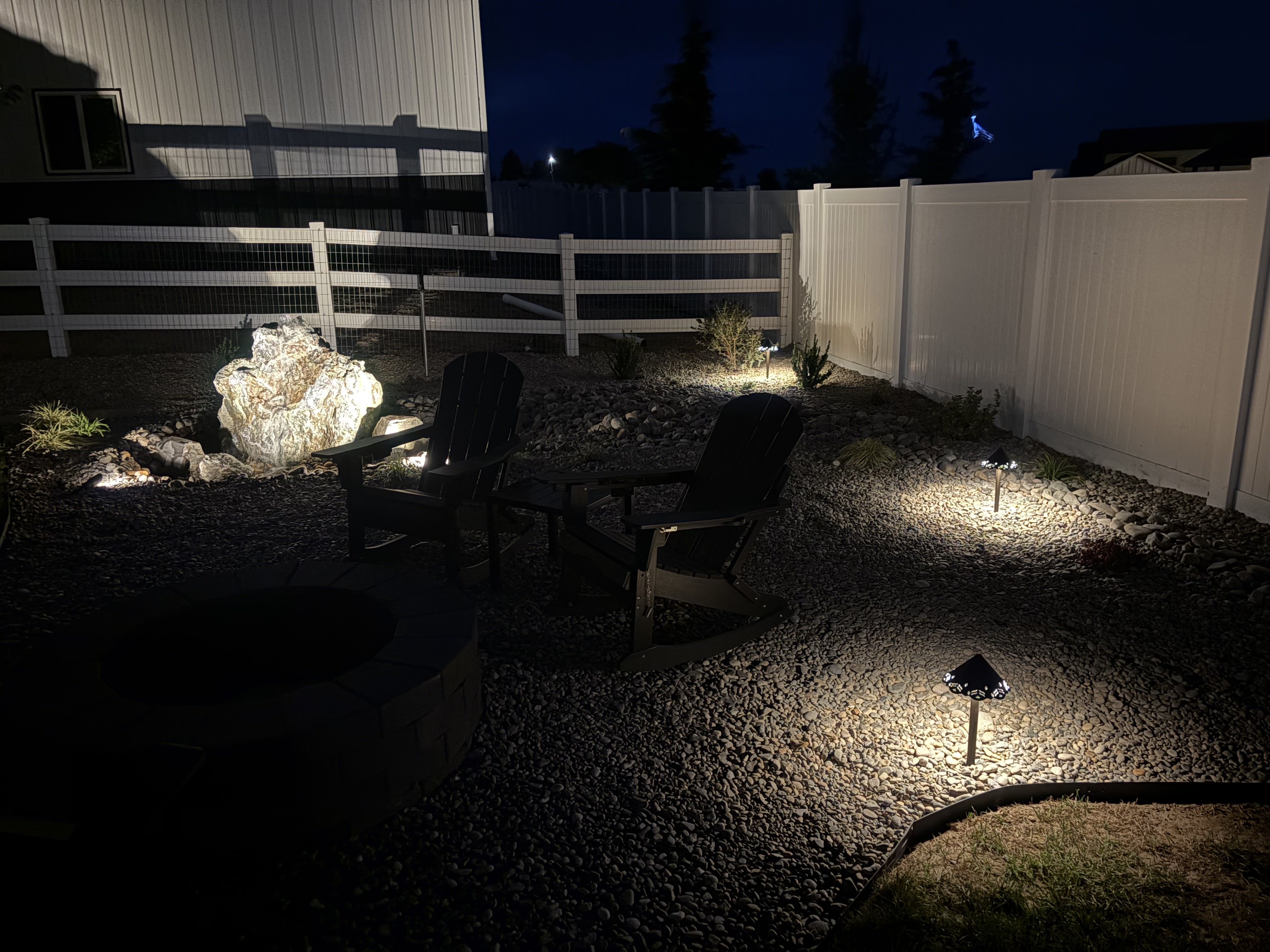 Project 04 finished backyard patio with fire pit, seating, and landscape lighting at night